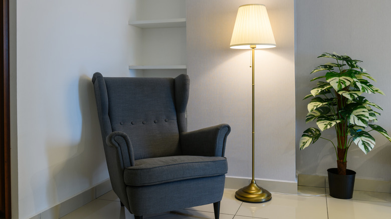 Lighted floor lamp beside gray chair and plant