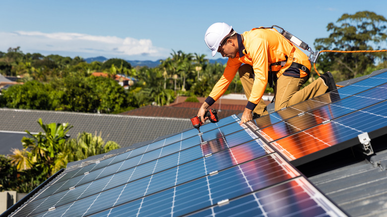 An installer uses a drill to mount solar panels on a roof