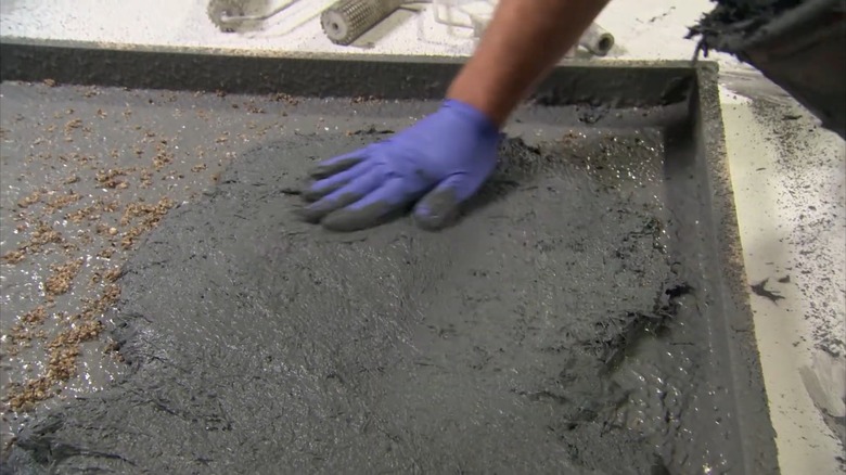 Gloved hand spreading poured concrete within a form