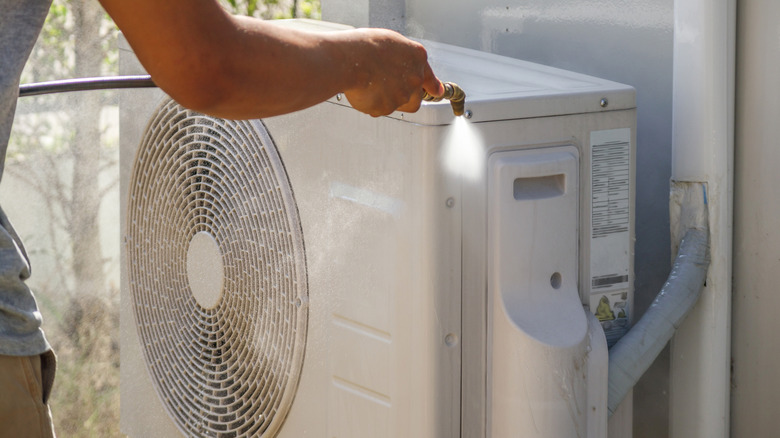 Person using hose to clean air conditioner condenser