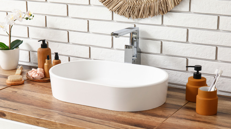 A white vessel sink surrounded by bathroom products in matching brown bottles.