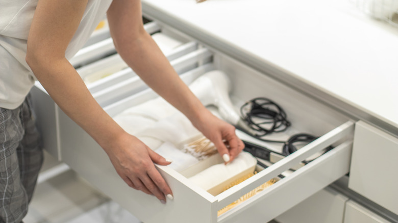 A number of products and appliances are being organized in a bathroom drawer.