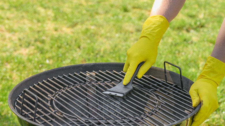 gleaning a barbecue grill with a grill tool and rubber gloves