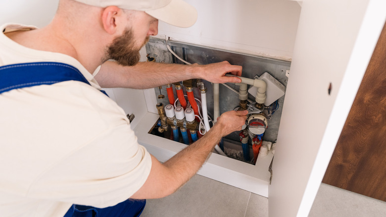 Male plumber inspecting water meter and pipes in an apartment