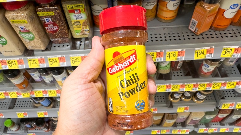 A hand holding a bottle of chili powder at grocery store