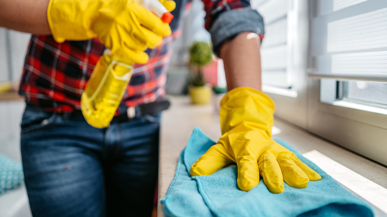 Person with yellow gloves dusting