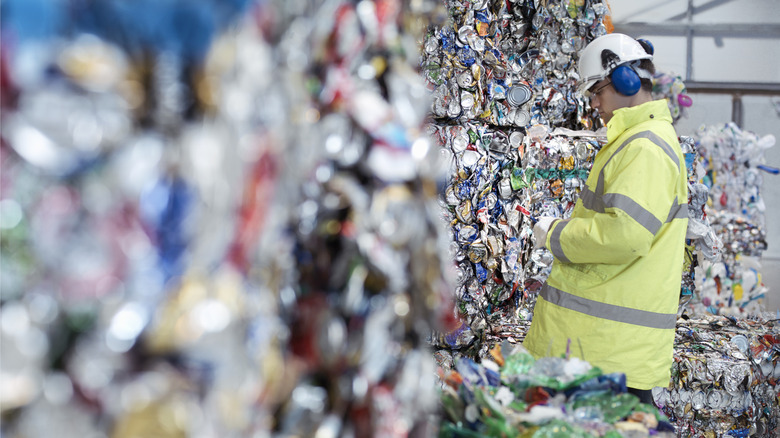 Man inspects crushed aluminum cans bound into a bale for recycling