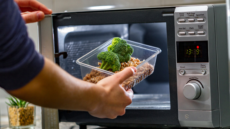 person putting plastic food container into microwave