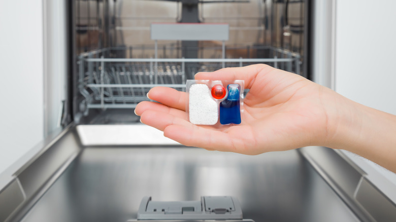 Hand holding up a dishwasher pod in front of an open dishwasher
