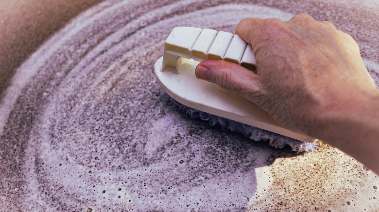 Man's hand cleaning a concrete surface with a scrub brush
