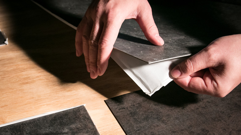 hands peeling adhesive tile