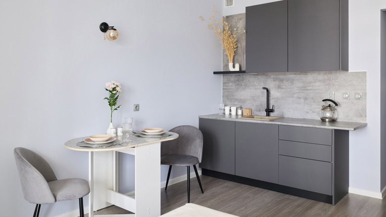 A tiny open kitchen features sleek gray cabinets and a small dinette with two upholstered chairs