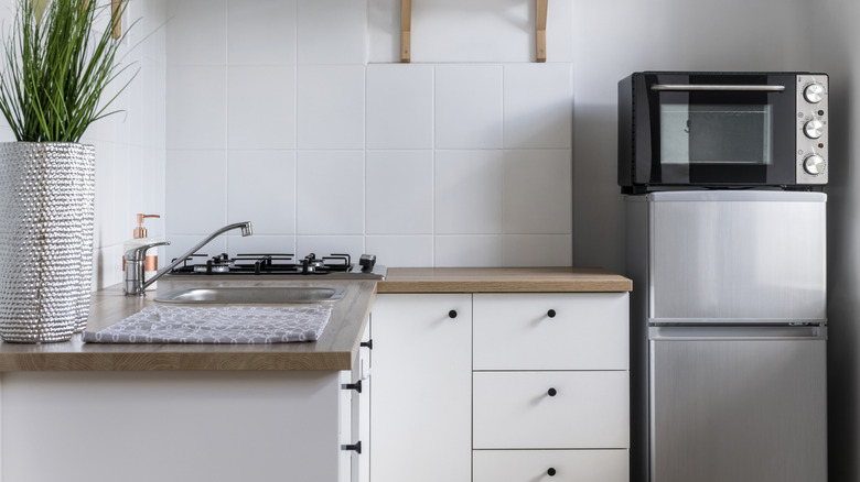 A microwave sits on top of a mini fridge in a small open kitchen