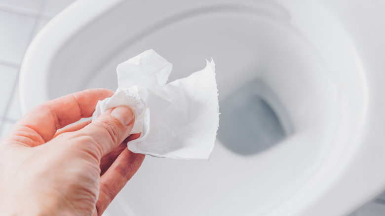 Person holding a square of toilet paper over toilet bowl