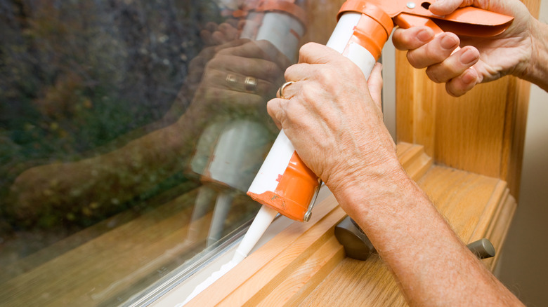 person caulking a window