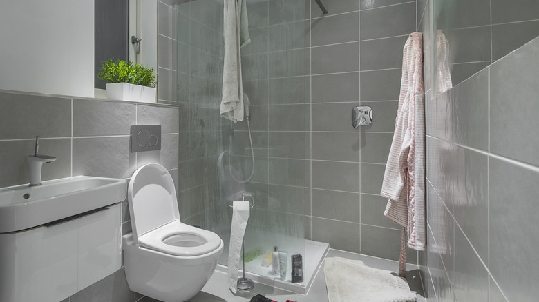 Messy bathroom with towel draped over shower glass.