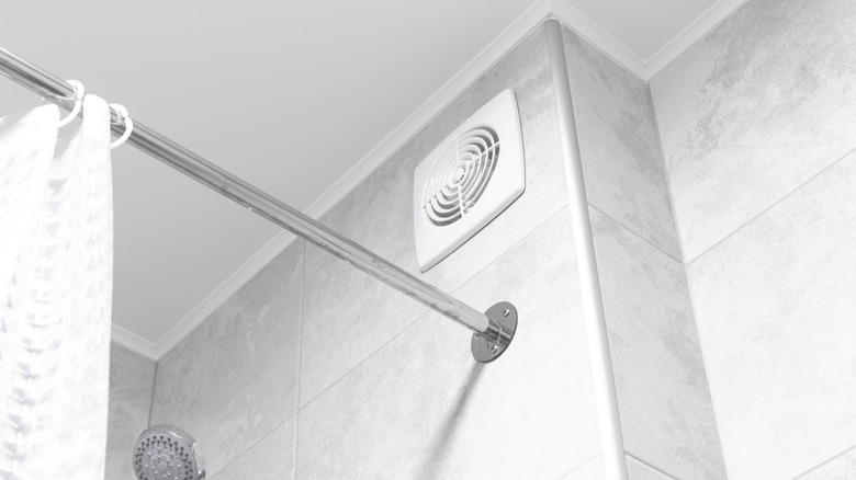 A bathroom exhaust vent above a shower curtain