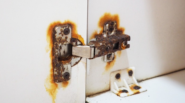 A severely rusty hinge on a white cabinet