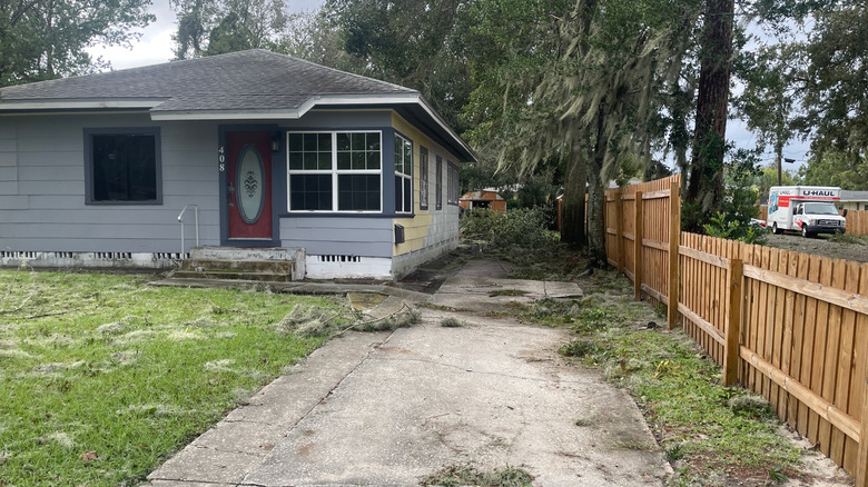 A flaking and cracked concrete driveway in front of a rundown house.