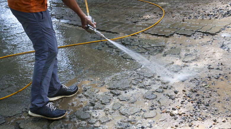 A person uses a pressure washer to remove loose material from a damaged concrete driveway.