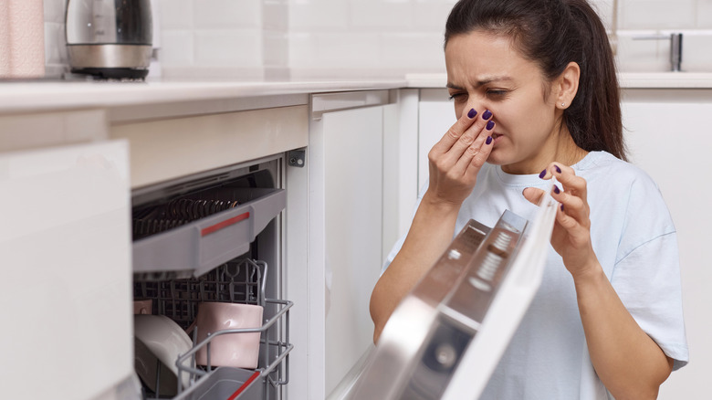 Woman smells strange and terrible smell coming from dishwasher machine in kitchen