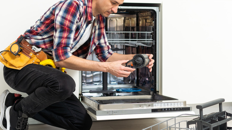 Handyman removing dirty dishwasher food residue filter