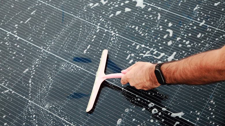 a person Cleaning Solar Panel with Shampoo and wiper