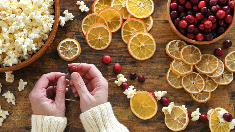 hands making a garland with dried oranges, cranberries and popcorn