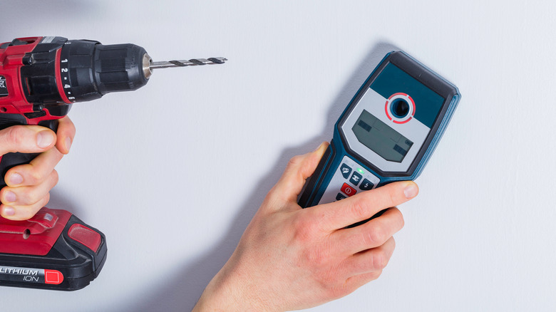 A person using a stud finder and holding a drill against a white wall
