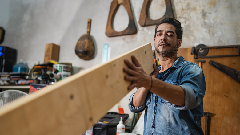 A man looking down a plank of wood to check for warping