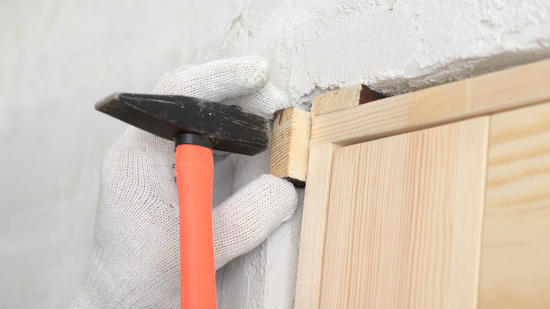 A gloved hand hammering a shim into a corner