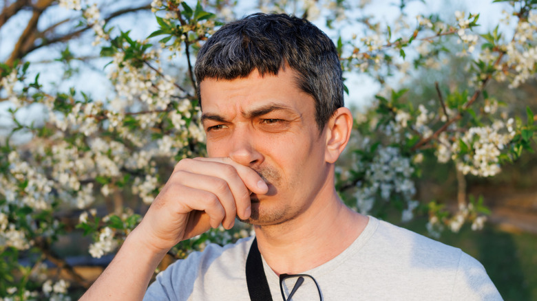 Man covers his nose near trees, reacting to a bad smell.