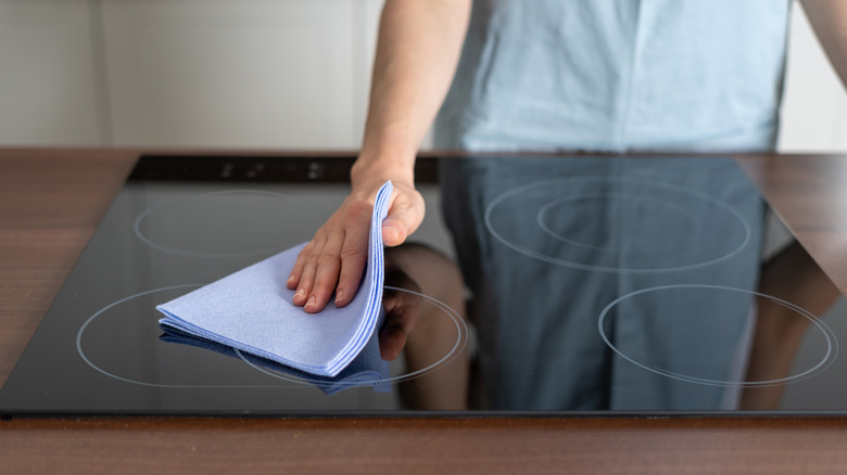 Person cleaning glass cooktop with blue cloth