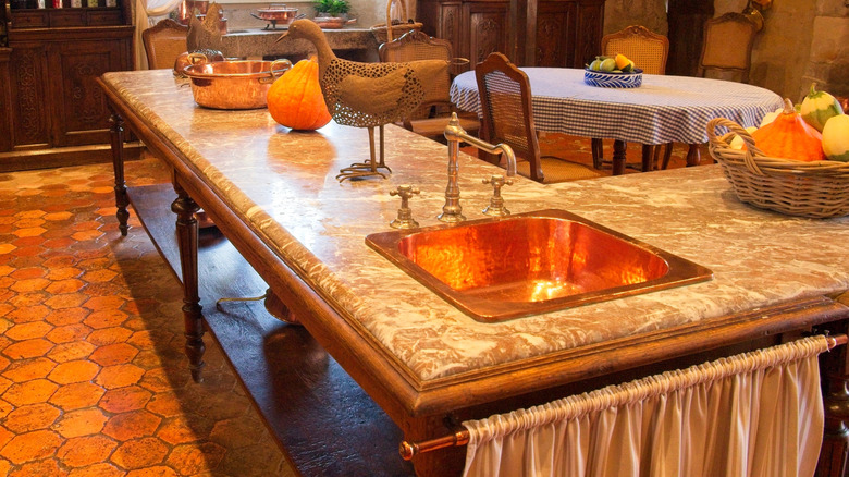 An old-fashioned kitchen with tiled floors, faux marble counter, and a cheap gold faucet and sink.