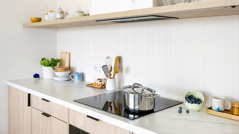 Modern kitchen counter with induction stovetop, utensils, and a bowl of blueberries