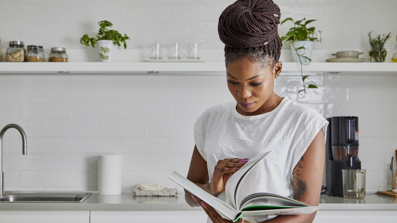 A woman flips through a cookbook in a minimally decorated kitchen.