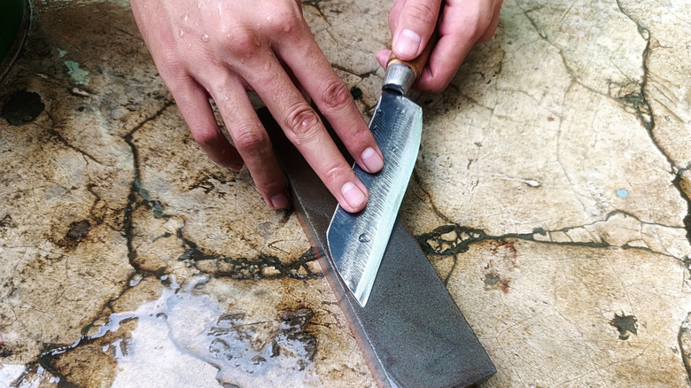 Hand sharpening knife on whetstone on floor