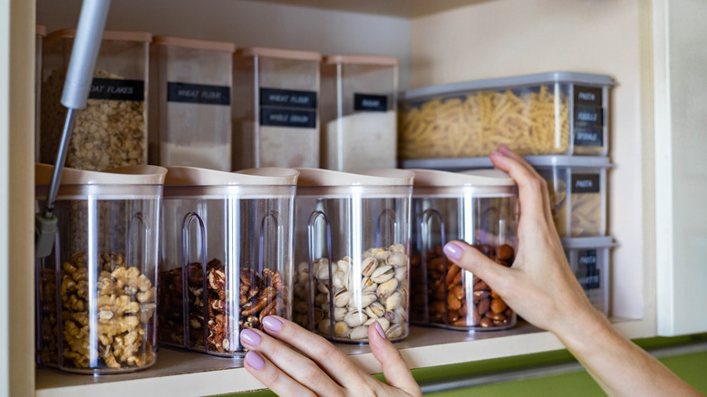 Closeup of woman's hands reaching for a storage container in a well-organized kitchen cabinet