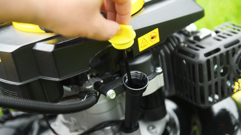 A person checks the oil on a lawn mower.