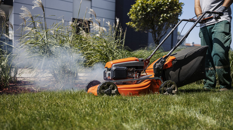 Man in teal pants with a smoking mower.