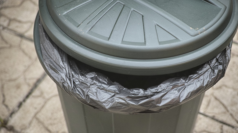 A forest green plastic trash can with a twistable lid and a black liner bag.