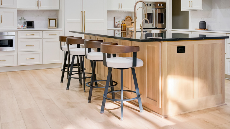 Beautiful new kitchen with white cabinets. The island has a farmhouse apron bowl sink. Light wooden floors cover the entire kitchen. Bar stools match the kitchen design. Golden hardware installed.