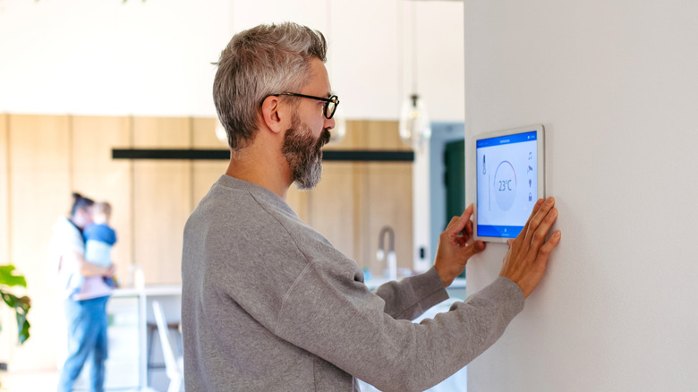 A man checking the digital display of a home thermostat.