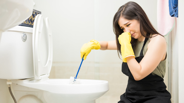 person cleaning toilet covering nose