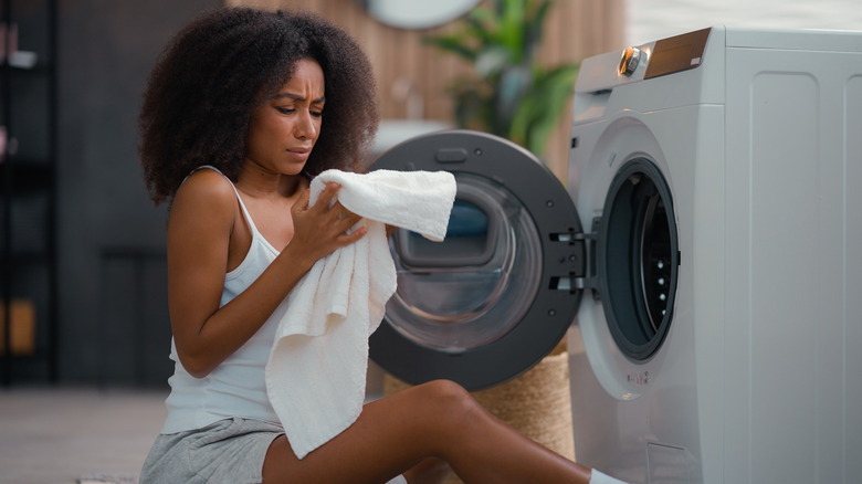 A woman looks concerned about the smell of a towel near an open front-load washing machine