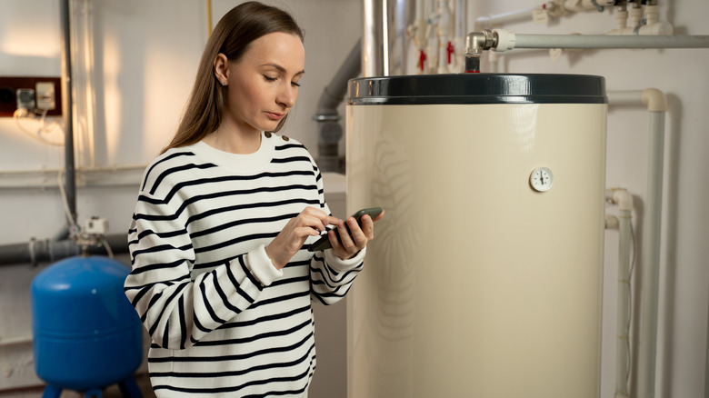 a woman inspecting a water heater and making notes on her phone