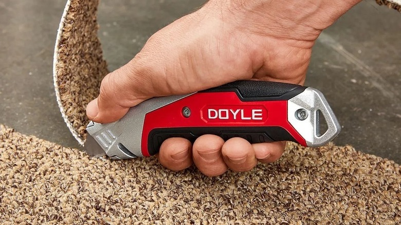 A man's hand slicing through carpet with the Doyle utility knife