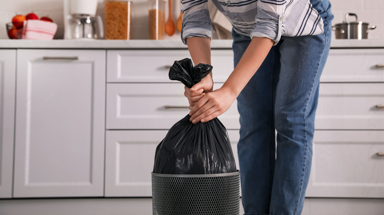 Person taking trash bag out of indoor bin in the kitchen