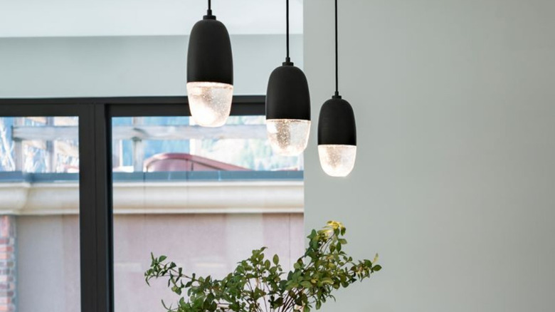 Three cast glass lighting fixtures hanging in a home with a sliding glass door in the background and a plant underneath