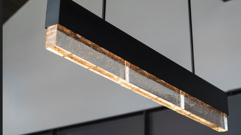 A simple rectangular cast glass chandelier with a soft yellow light hanging from a ceiling